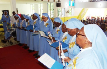 Several sisters standing side-by-side holding folders and candles dressed in blue