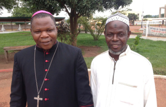 Two African men standing besides each other with one wearing white and the other in Cardinal's black clothing