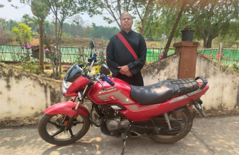 Priest standing next to his new motorcycle provided by ACN.