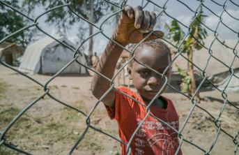 A young child looking through a fence around a displacement camp